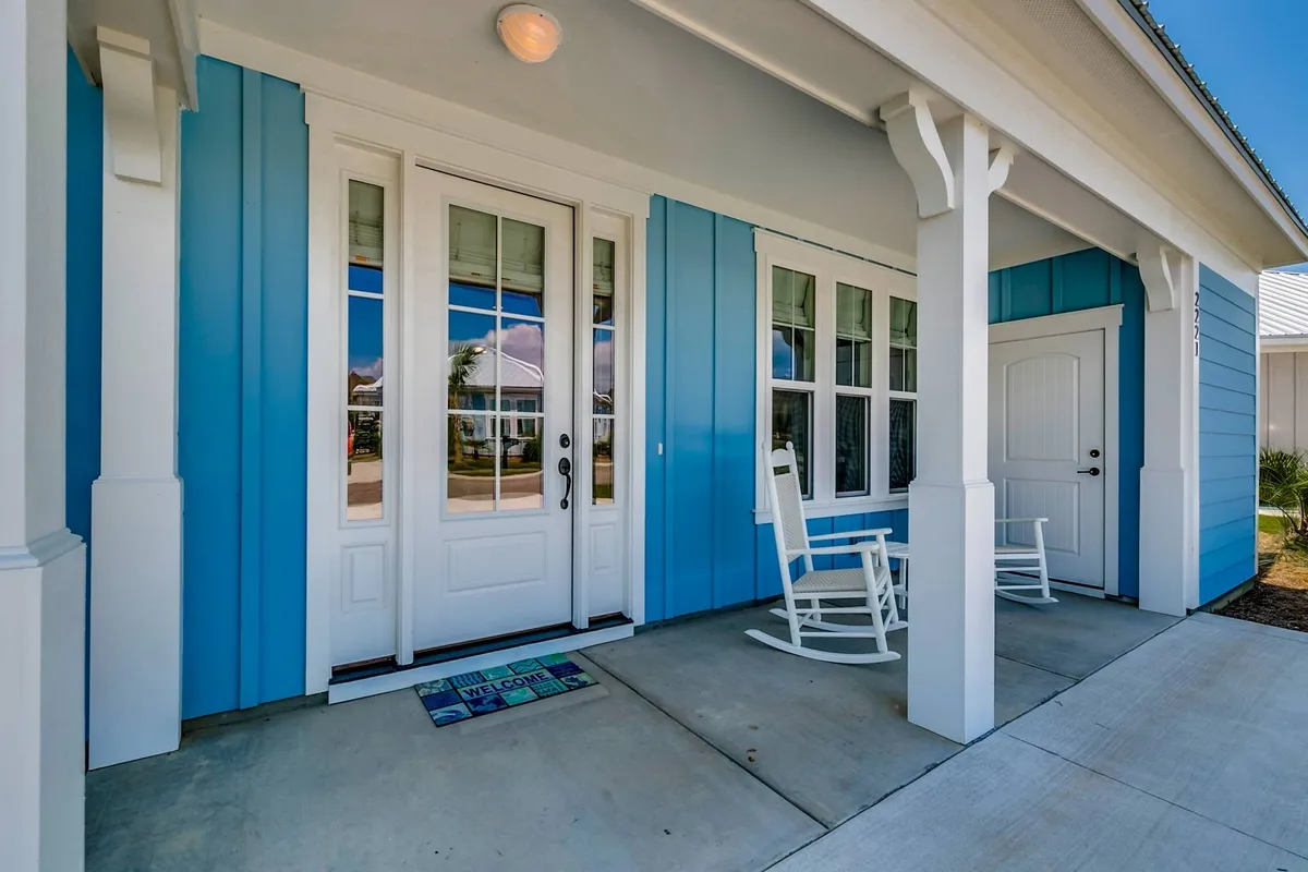 The image shows the bungalow's charming front porch featuring classic rocking chairs, blue siding, and a welcoming front door. The space is styled for comfort and relaxation, offering a tranquil spot that is perfect for enjoying the fresh air and greeting guests as they arrive.
