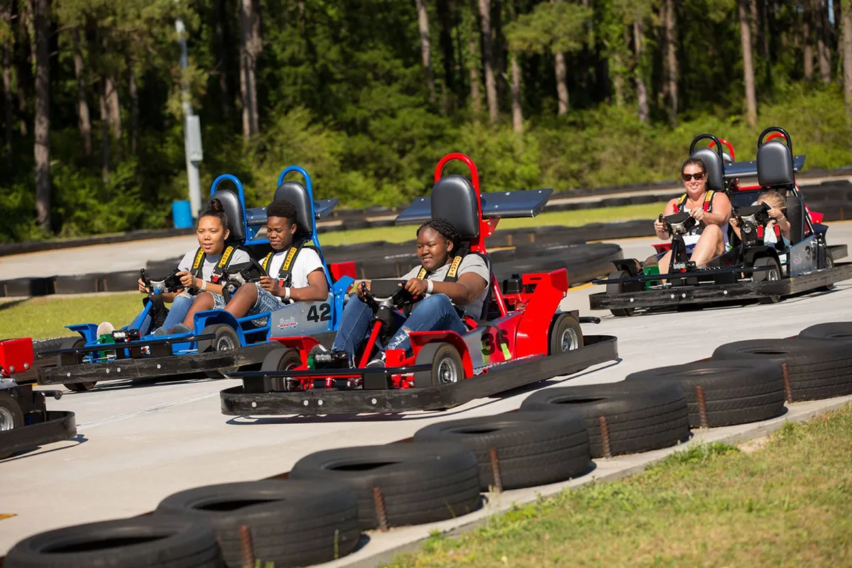 A dynamic exterior scene featuring families and kids zipping around a go-kart track, with smiling participants and a buzz of friendly competition. The image captures the thrill and excitement of outdoor activities available nearby, emphasizing action and shared joy.