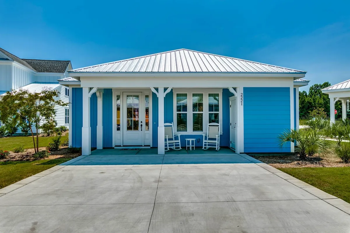 A charming blue bungalow with white rocking chairs welcoming guests to its classic front porch, framed by a symmetrical entrance and surrounded by a peaceful yard—perfect for gatherings and relaxation.