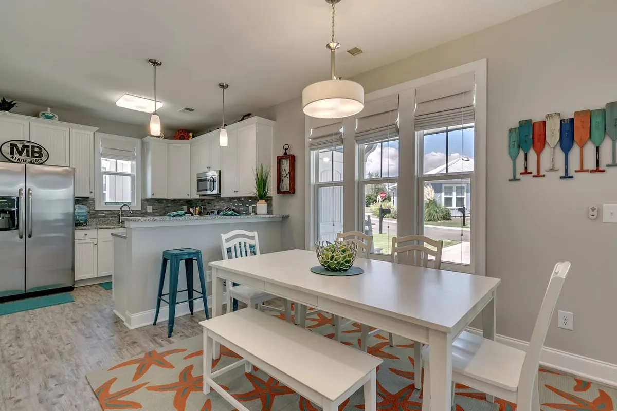 An inviting view of the kitchen and dining area, featuring a dining table, kitchen island, stainless steel refrigerator, and decorative oars on the wall. The setup is cheerful, with ample space for meal prep and family conversation.