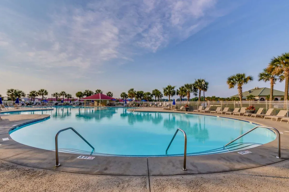 This image features a large, inviting swimming pool surrounded by palm trees and lounge chairs. The setting is leisurely, with hints of sunset lighting and ample space for guests to relax and unwind poolside.