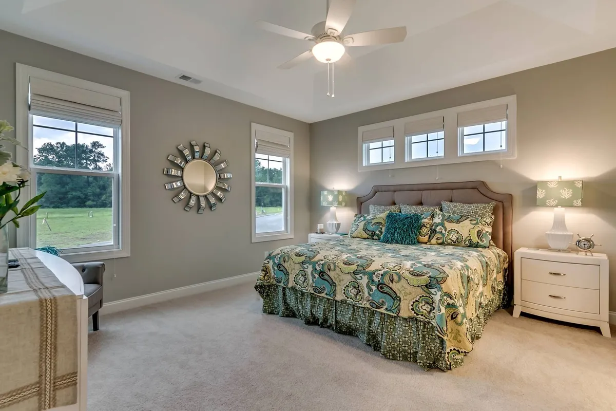 A tranquil bedroom scene featuring a neatly made bed with decorative bedding, flanked by bedside lamps and a wall-mounted mirror. The space is brightened by natural light filtering through a nearby window, creating a serene and cozy sanctuary ideal for rest and relaxation.